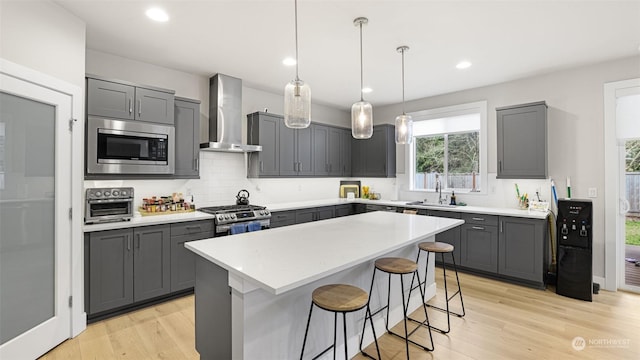 kitchen featuring light hardwood / wood-style floors, a kitchen island, gray cabinetry, stainless steel appliances, and wall chimney exhaust hood