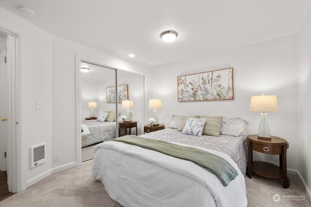 bedroom with heating unit, light colored carpet, and a closet