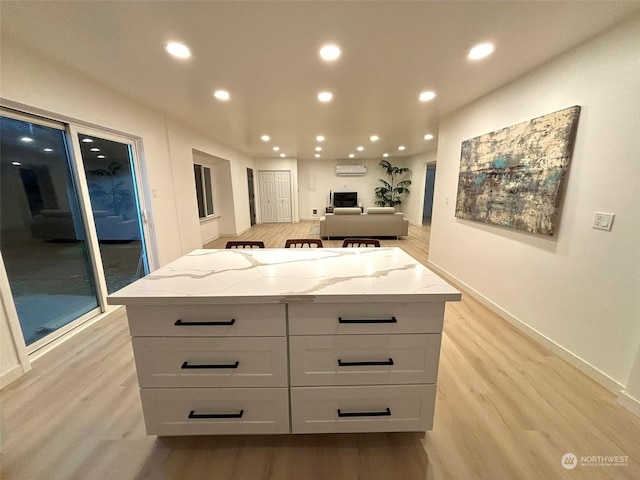 kitchen featuring light wood-type flooring, light stone countertops, a wall unit AC, and a center island