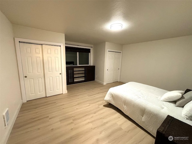 bedroom featuring a textured ceiling, light wood-type flooring, and multiple closets