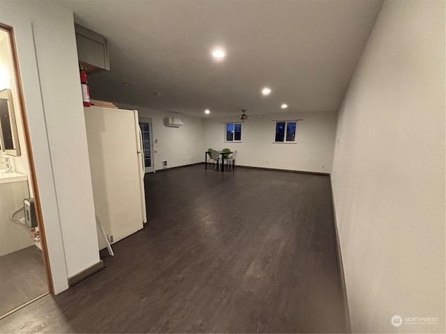 basement with a wall mounted AC, dark hardwood / wood-style flooring, and white fridge