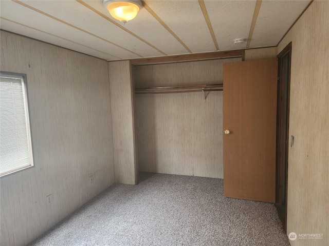 unfurnished bedroom featuring carpet, a closet, and wooden walls