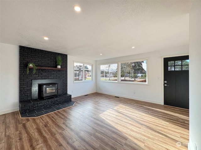 unfurnished living room featuring a textured ceiling, a wood stove, and hardwood / wood-style floors