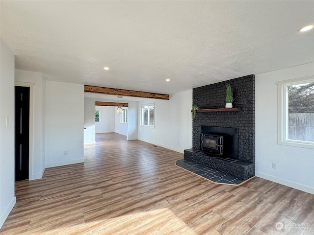 unfurnished living room featuring a wood stove, a textured ceiling, light hardwood / wood-style flooring, and beamed ceiling