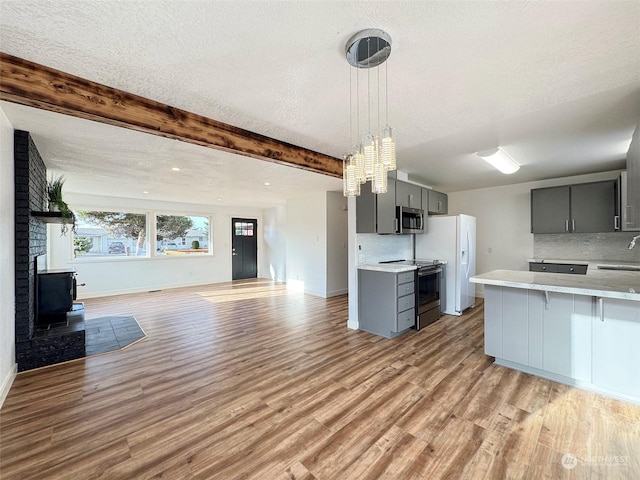 kitchen with appliances with stainless steel finishes, beamed ceiling, backsplash, kitchen peninsula, and gray cabinetry