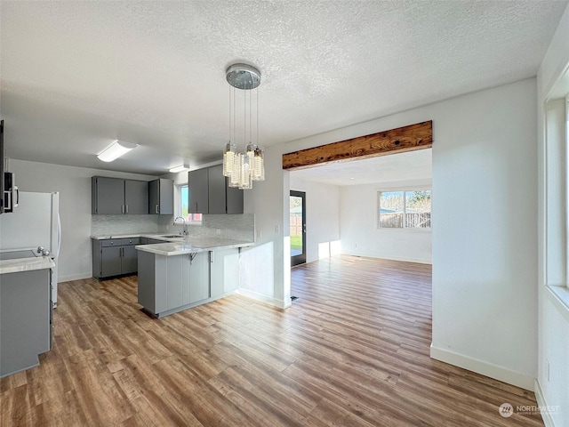 kitchen featuring hardwood / wood-style floors, kitchen peninsula, gray cabinets, decorative backsplash, and sink