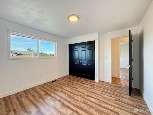 unfurnished bedroom featuring a textured ceiling, a closet, and light hardwood / wood-style flooring