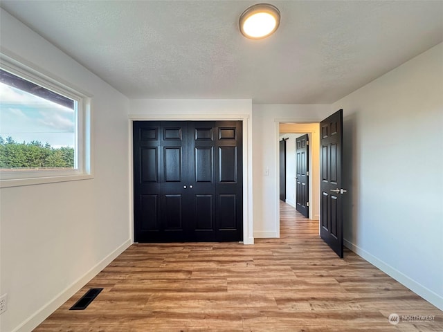 unfurnished bedroom featuring light hardwood / wood-style floors, a textured ceiling, and a closet