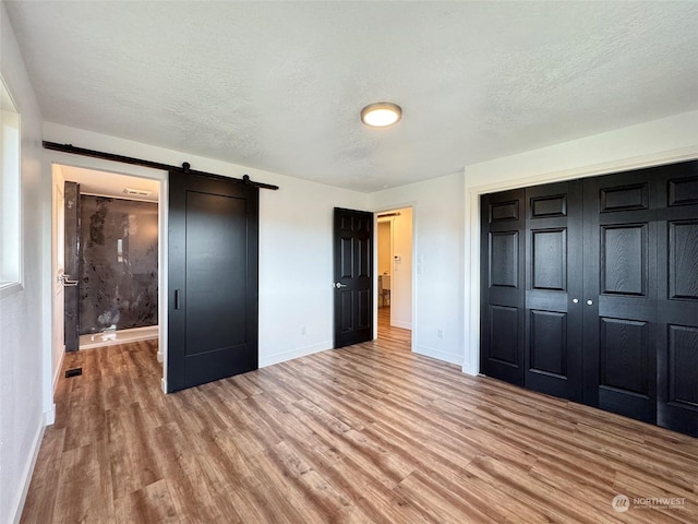 unfurnished bedroom with hardwood / wood-style floors, a closet, a textured ceiling, and a barn door