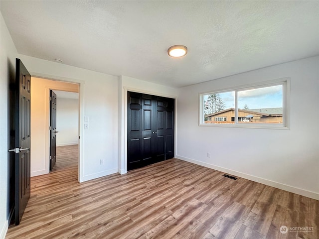 unfurnished bedroom featuring light wood-type flooring, a closet, and a textured ceiling