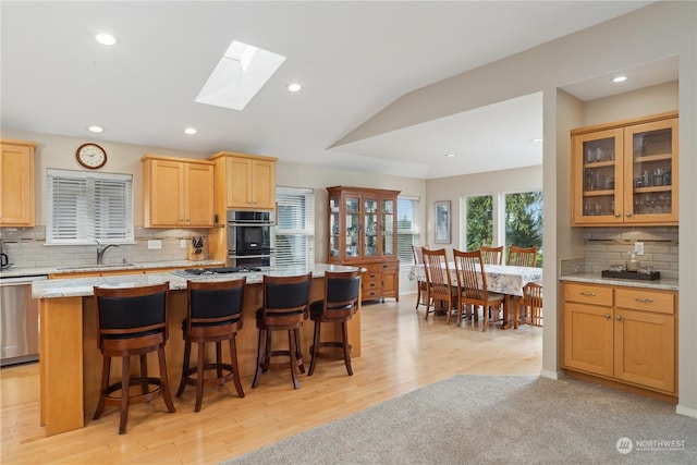 kitchen with sink, stainless steel appliances, a center island, light stone counters, and a kitchen bar