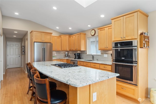 kitchen featuring vaulted ceiling, a kitchen island, appliances with stainless steel finishes, a kitchen breakfast bar, and light stone counters