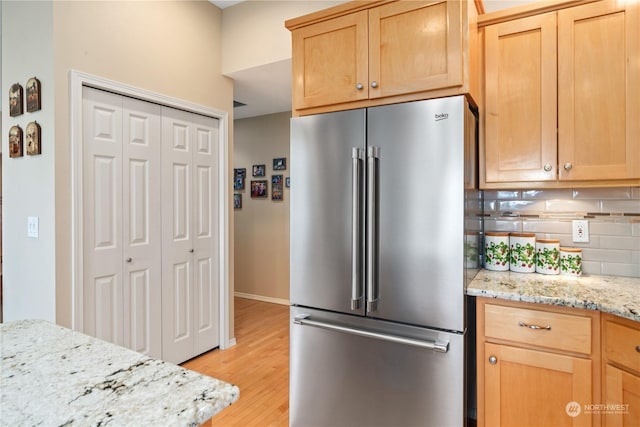 kitchen with backsplash, light stone counters, high end fridge, light brown cabinets, and light hardwood / wood-style flooring