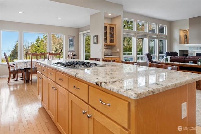 kitchen with a center island, stainless steel gas cooktop, light stone counters, and light hardwood / wood-style floors