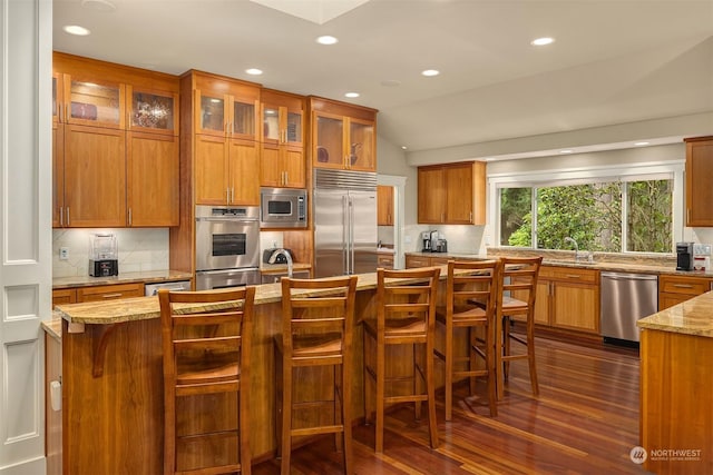 kitchen with light stone counters, a breakfast bar area, lofted ceiling, and built in appliances