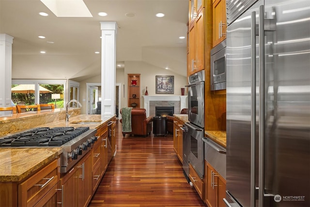 kitchen with vaulted ceiling with skylight, dark wood-type flooring, stainless steel appliances, sink, and light stone counters