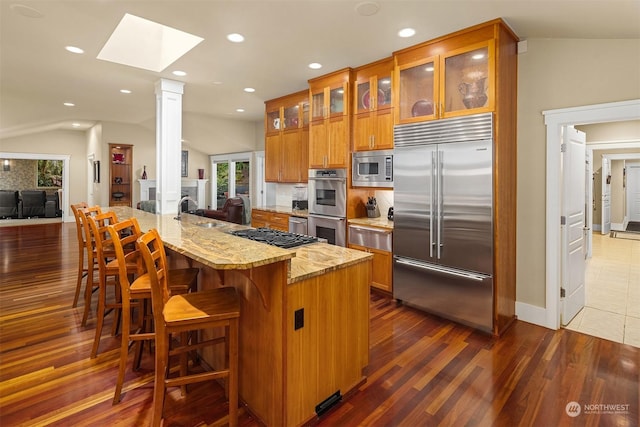 kitchen with light stone counters, vaulted ceiling with skylight, backsplash, and built in appliances