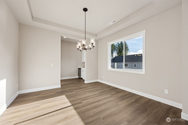 unfurnished dining area with hardwood / wood-style flooring, a tray ceiling, and an inviting chandelier