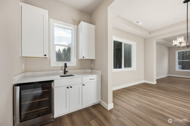 bar with hardwood / wood-style floors, wine cooler, hanging light fixtures, white cabinets, and sink