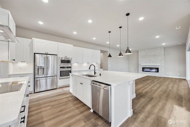 kitchen with white cabinets, a kitchen island with sink, a stone fireplace, and stainless steel appliances