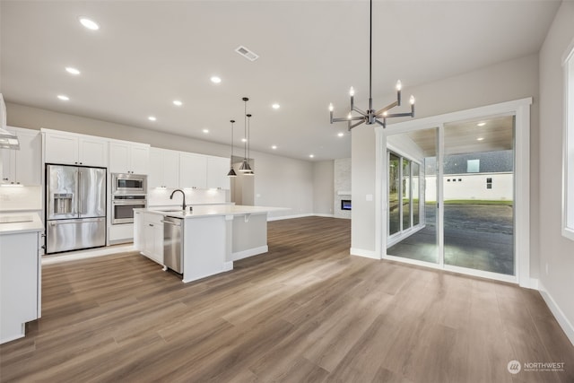 kitchen with a center island with sink, stainless steel appliances, wood-type flooring, hanging light fixtures, and sink