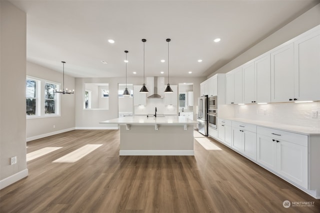 kitchen featuring pendant lighting, an inviting chandelier, hardwood / wood-style flooring, white cabinets, and wall chimney exhaust hood