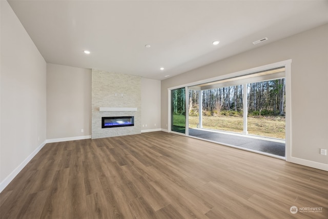 unfurnished living room with hardwood / wood-style floors and a stone fireplace