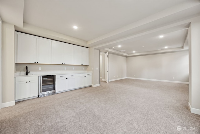 kitchen featuring white cabinets, beverage cooler, light carpet, sink, and a raised ceiling