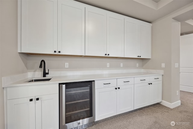 kitchen with sink, white cabinetry, beverage cooler, and light colored carpet