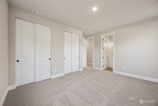 unfurnished bedroom with ensuite bath, multiple closets, and light carpet