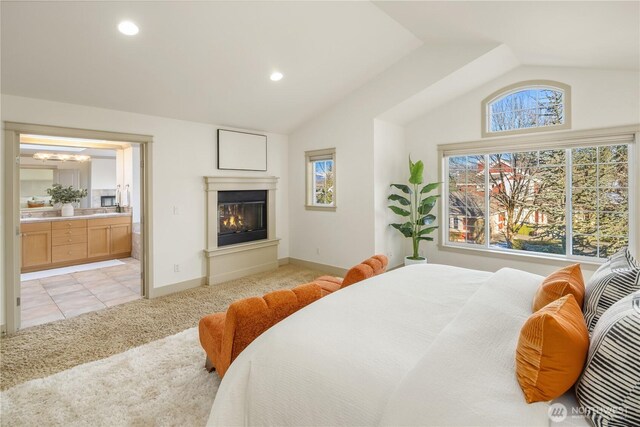 bedroom with vaulted ceiling, ensuite bath, light carpet, and a glass covered fireplace