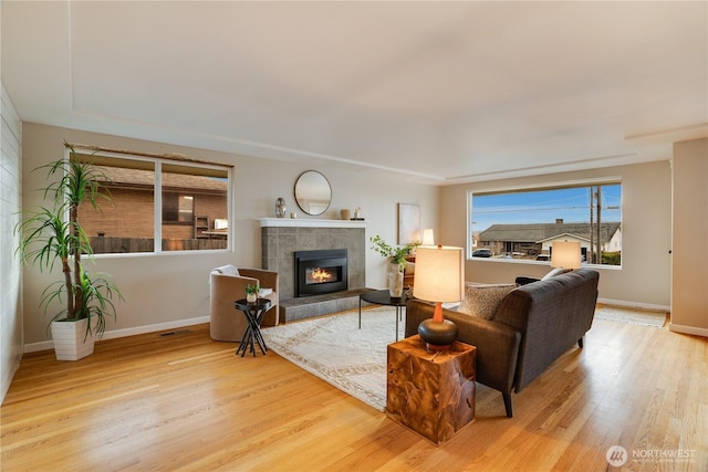 living area featuring visible vents, baseboards, wood finished floors, and a tiled fireplace