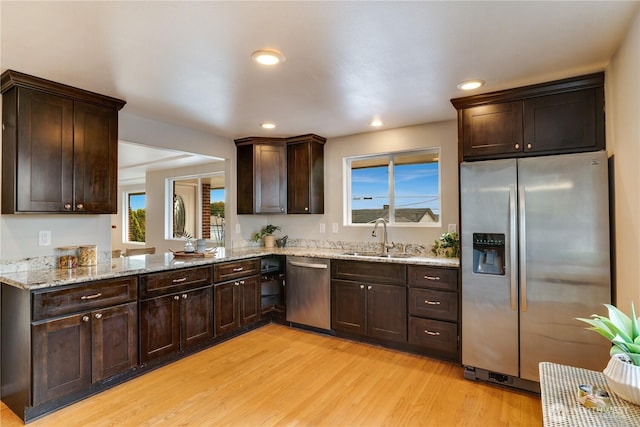 kitchen with light stone countertops, a sink, stainless steel appliances, dark brown cabinets, and light wood-type flooring