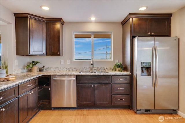 kitchen with dark brown cabinets, light wood-style flooring, appliances with stainless steel finishes, and a sink