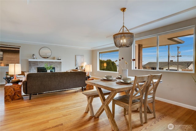 dining area featuring a tiled fireplace, a notable chandelier, wood finished floors, and baseboards