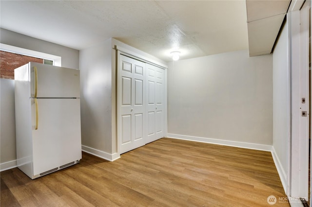 interior space featuring baseboards, light wood-type flooring, and a textured ceiling