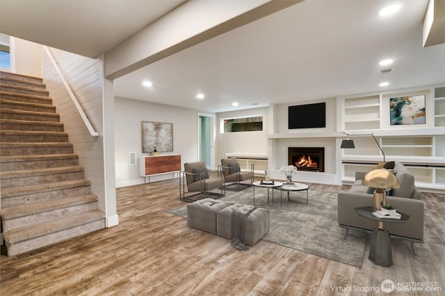 living room with recessed lighting, a warm lit fireplace, stairs, and wood finished floors