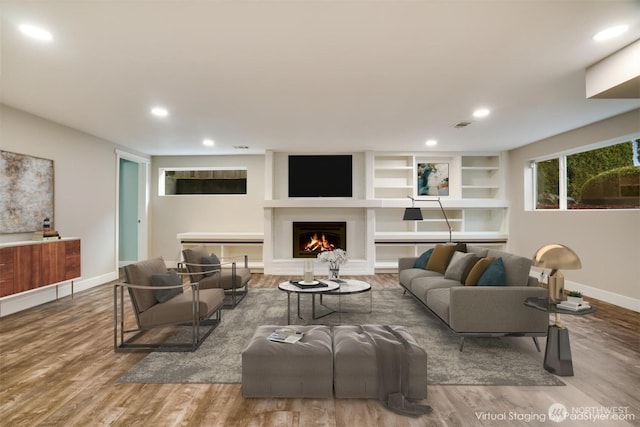 living room featuring recessed lighting, baseboards, a warm lit fireplace, and wood finished floors