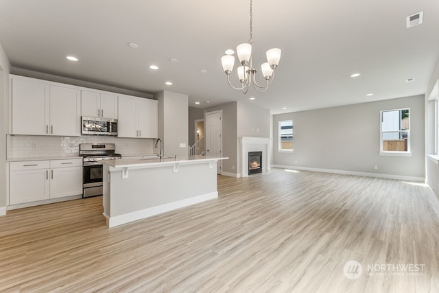 kitchen with appliances with stainless steel finishes, pendant lighting, white cabinetry, and tasteful backsplash