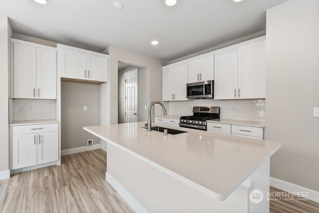 kitchen featuring sink, white cabinetry, appliances with stainless steel finishes, and a center island with sink