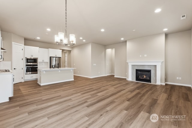 unfurnished living room featuring a premium fireplace, a chandelier, and light hardwood / wood-style flooring