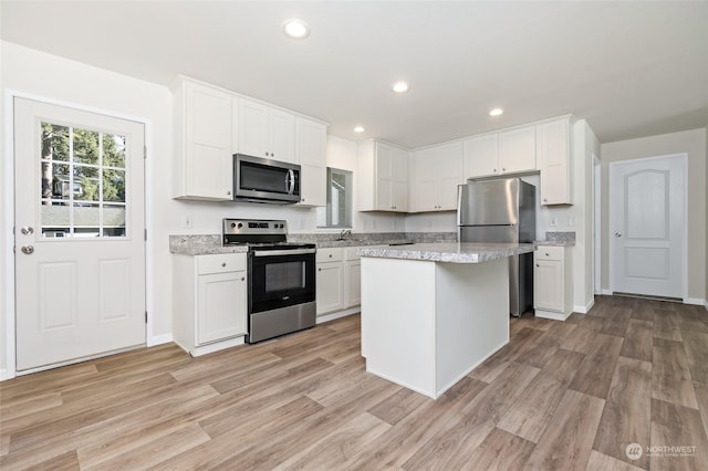 kitchen with stainless steel appliances, a center island, white cabinets, and light wood-type flooring