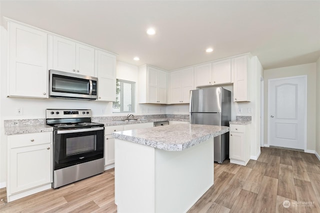 kitchen with white cabinetry, stainless steel appliances, a center island, and light hardwood / wood-style flooring