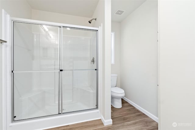 bathroom with hardwood / wood-style flooring, toilet, and a shower with door