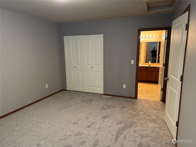 unfurnished bedroom with light carpet, a closet, ensuite bath, and sink