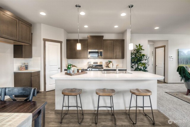 kitchen with stainless steel appliances, a kitchen island with sink, dark wood-type flooring, pendant lighting, and sink