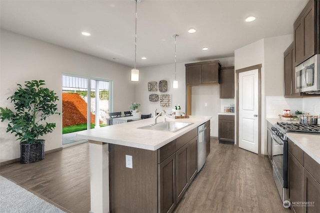 kitchen with appliances with stainless steel finishes, dark wood-type flooring, sink, hanging light fixtures, and a center island with sink