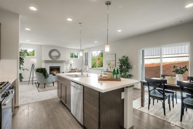 kitchen with dark brown cabinetry, appliances with stainless steel finishes, a fireplace, sink, and a kitchen island with sink