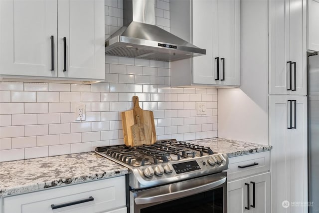 kitchen with stainless steel gas range oven, white cabinetry, light stone counters, decorative backsplash, and wall chimney range hood