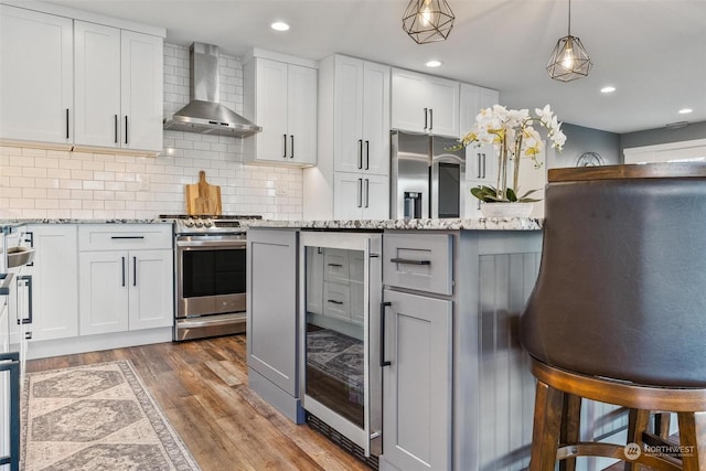 kitchen with tasteful backsplash, white cabinetry, light stone counters, stainless steel appliances, and wall chimney exhaust hood